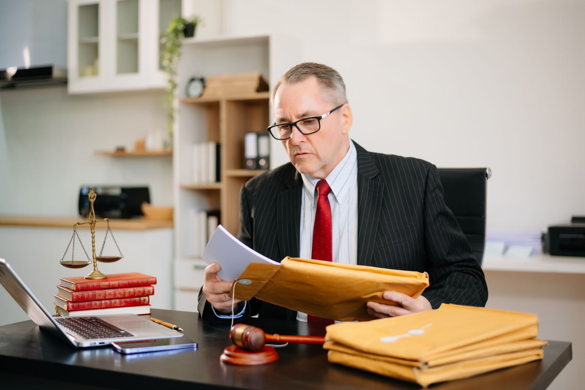 A professional in a suit and red tie reviews legal documents at a desk with a scale of justice, a gavel, and paperwork.