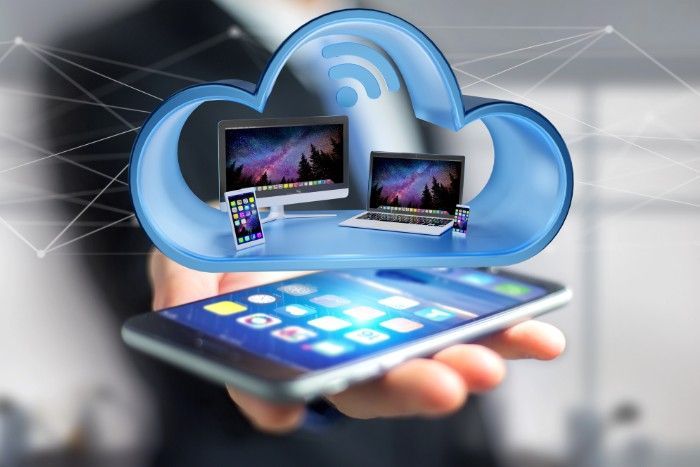 Hand holding a smartphone, with a cloud icon containing laptop, phone, and computer devices.
