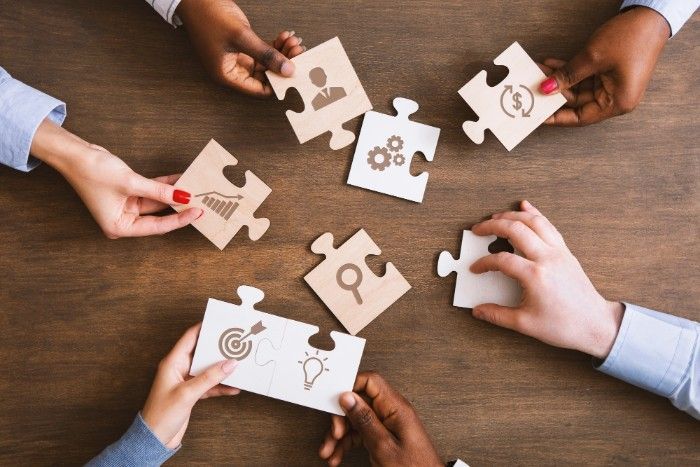 Hands holding puzzle pieces with icons, symbolizing teamwork and goals on a wooden table.