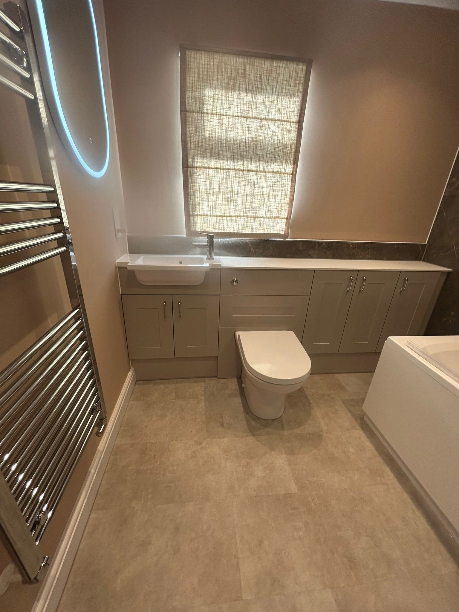 Bathroom with gray tile, toilet, vanity, heated towel rack, and textured window shade.