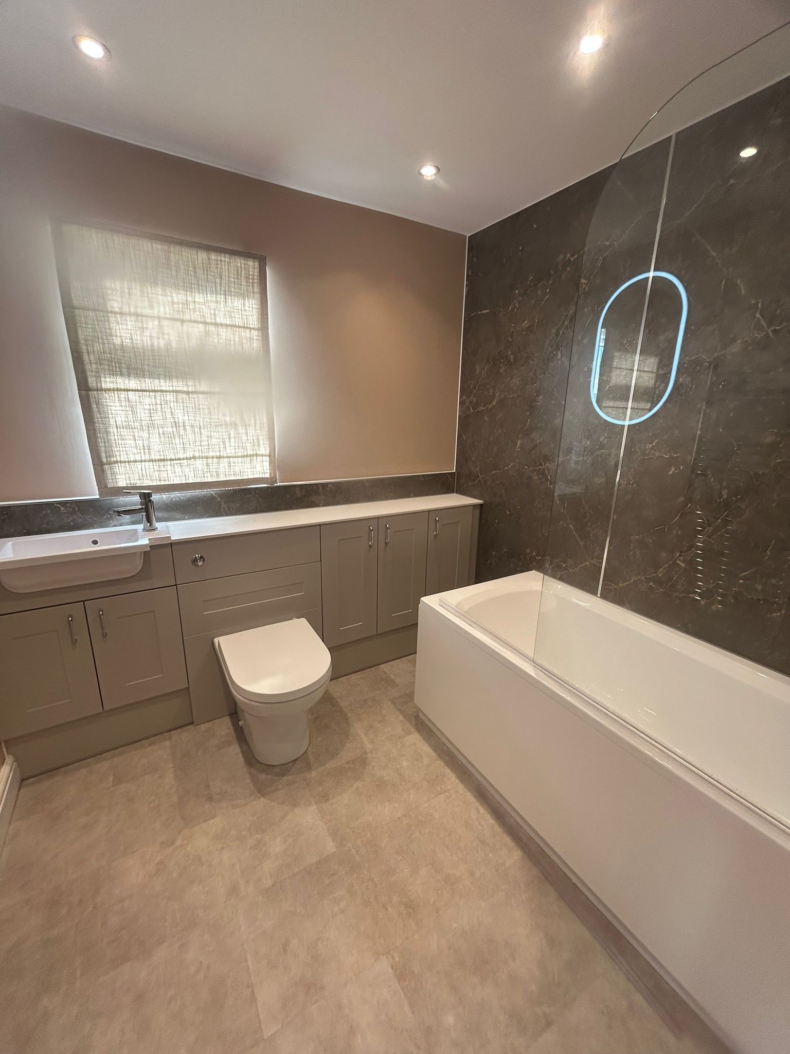 Modern bathroom with gray cabinets, toilet, bathtub, and large dark tile accent wall.