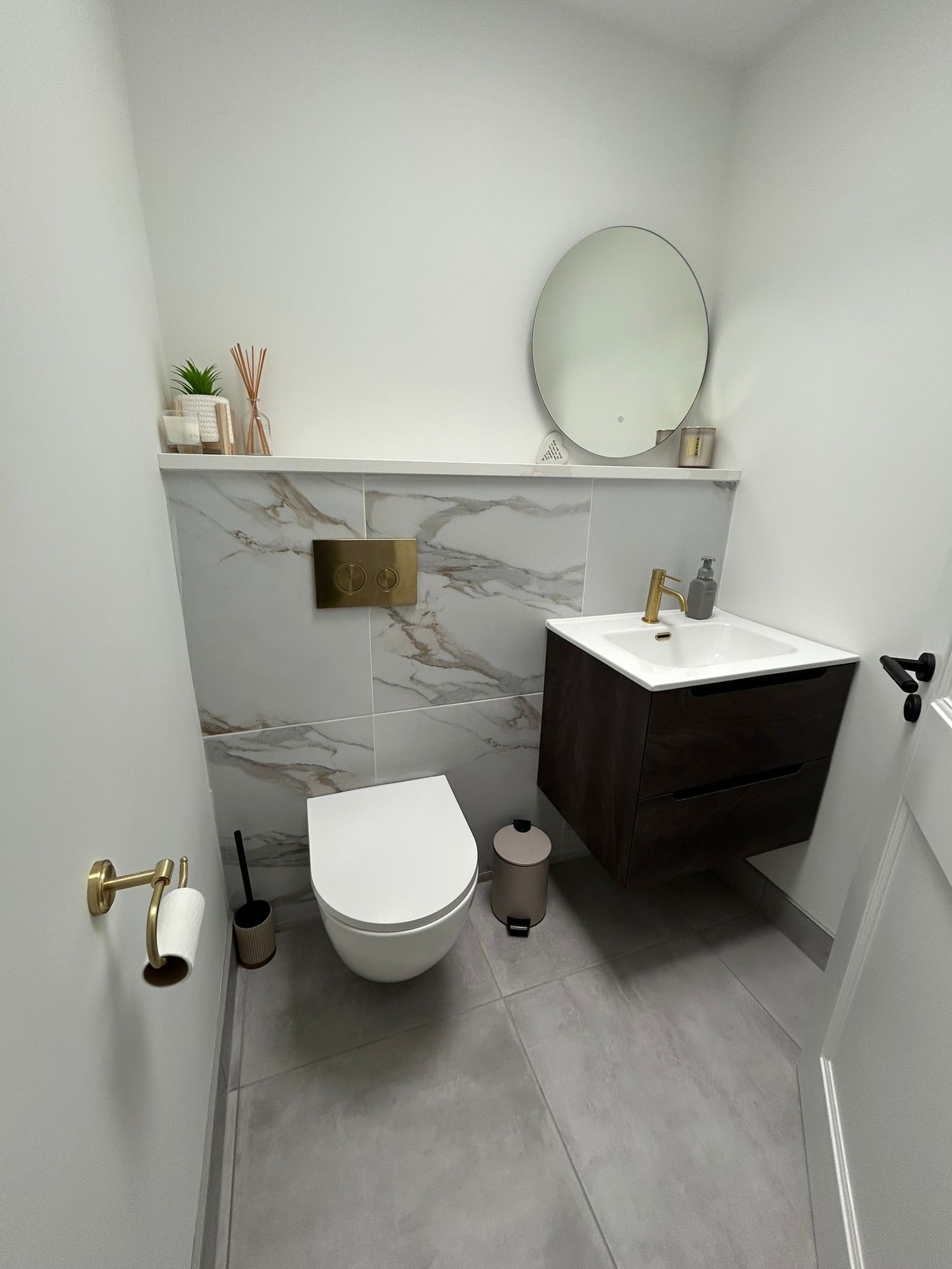Modern bathroom with floating wood vanity, white toilet, marble backsplash, and gold fixtures.