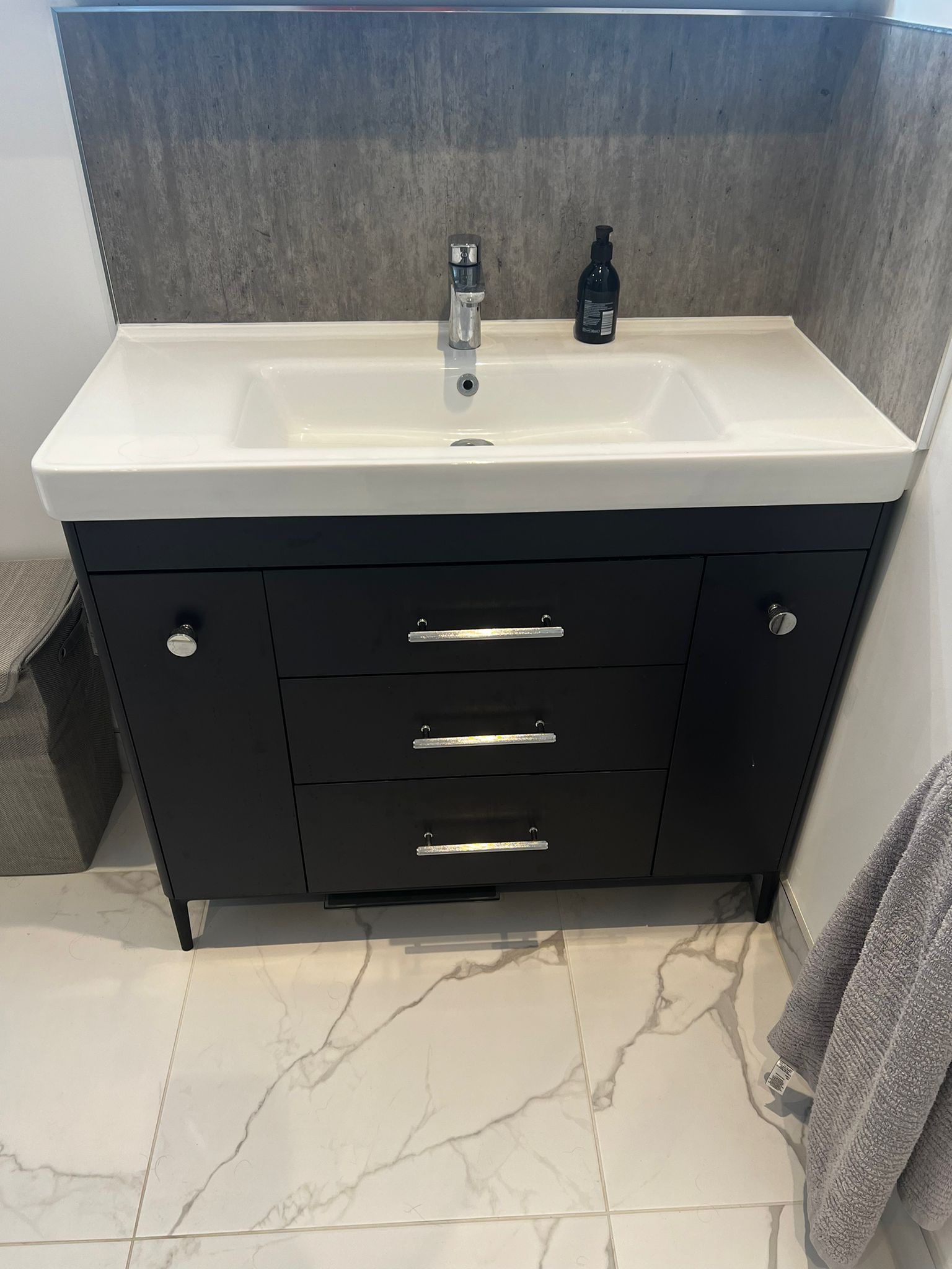 Black vanity with white sink and chrome fixtures. Marble tile floor, gray wall.