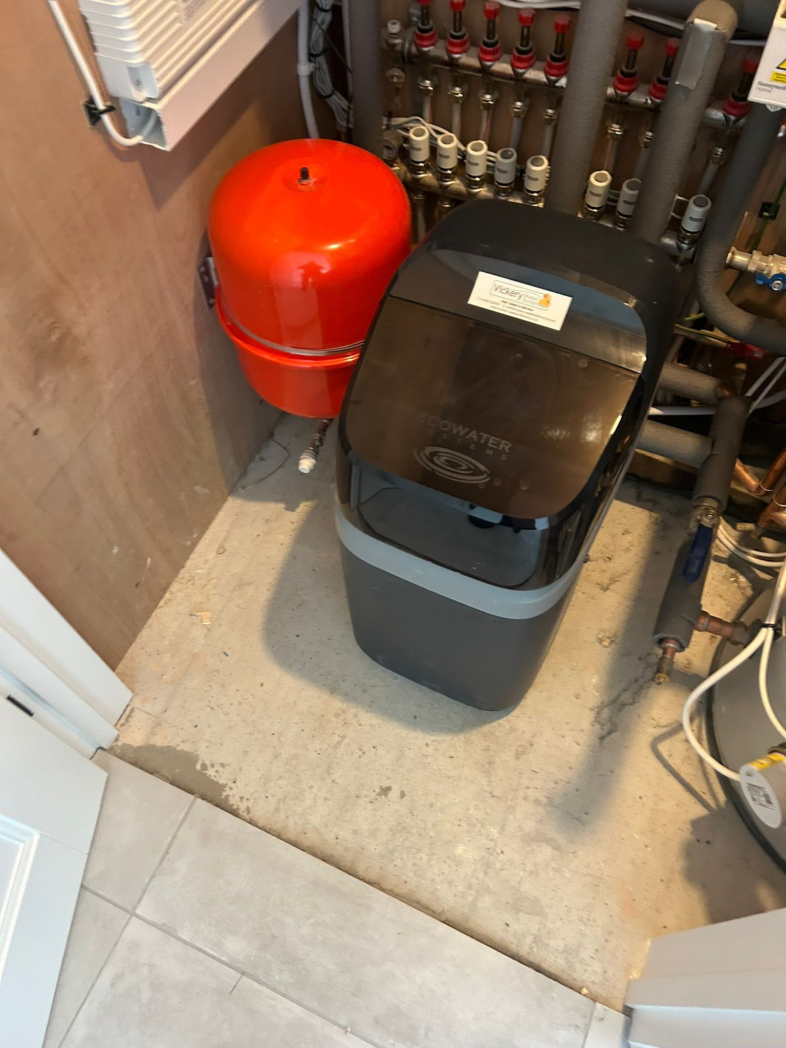 Red expansion tank and black water softener in a utility room.