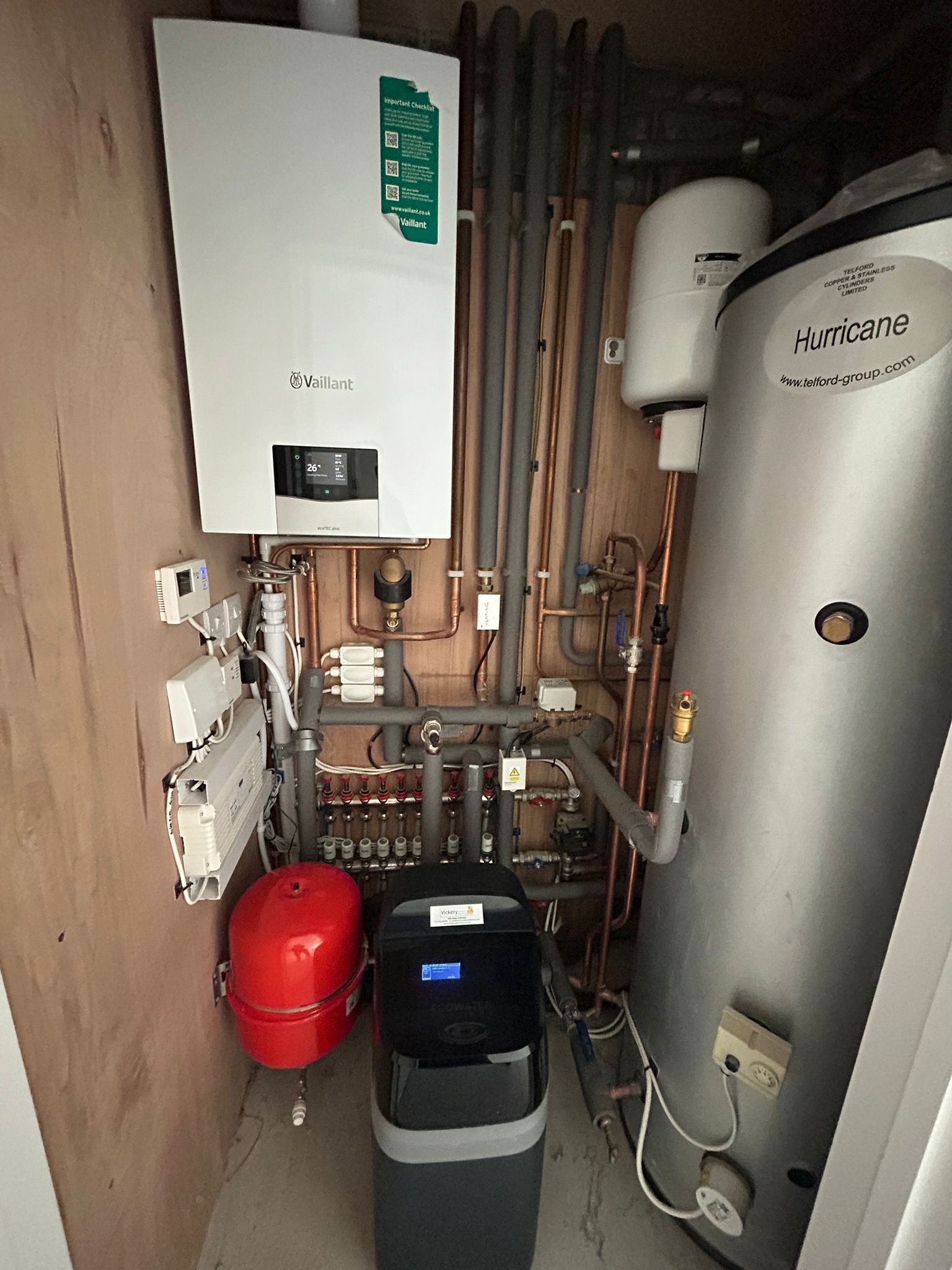 Heating system: white boiler, water tank, red expansion tank, pipes, and water softener in a utility closet.