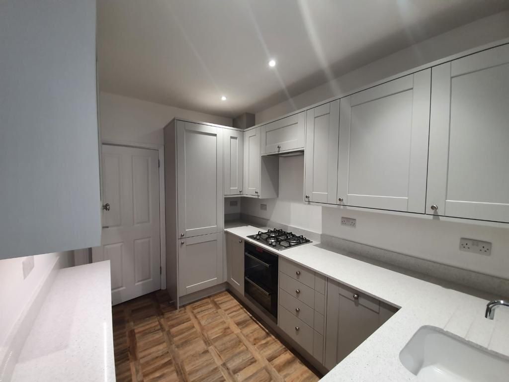 Gray kitchen cabinets, white countertops, a gas stove, and wooden flooring.
