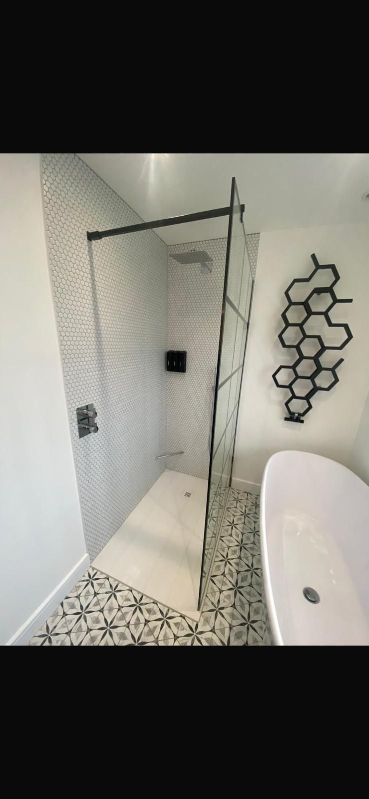Modern bathroom with a glass shower, white walls, and patterned floor. A white tub sits nearby.