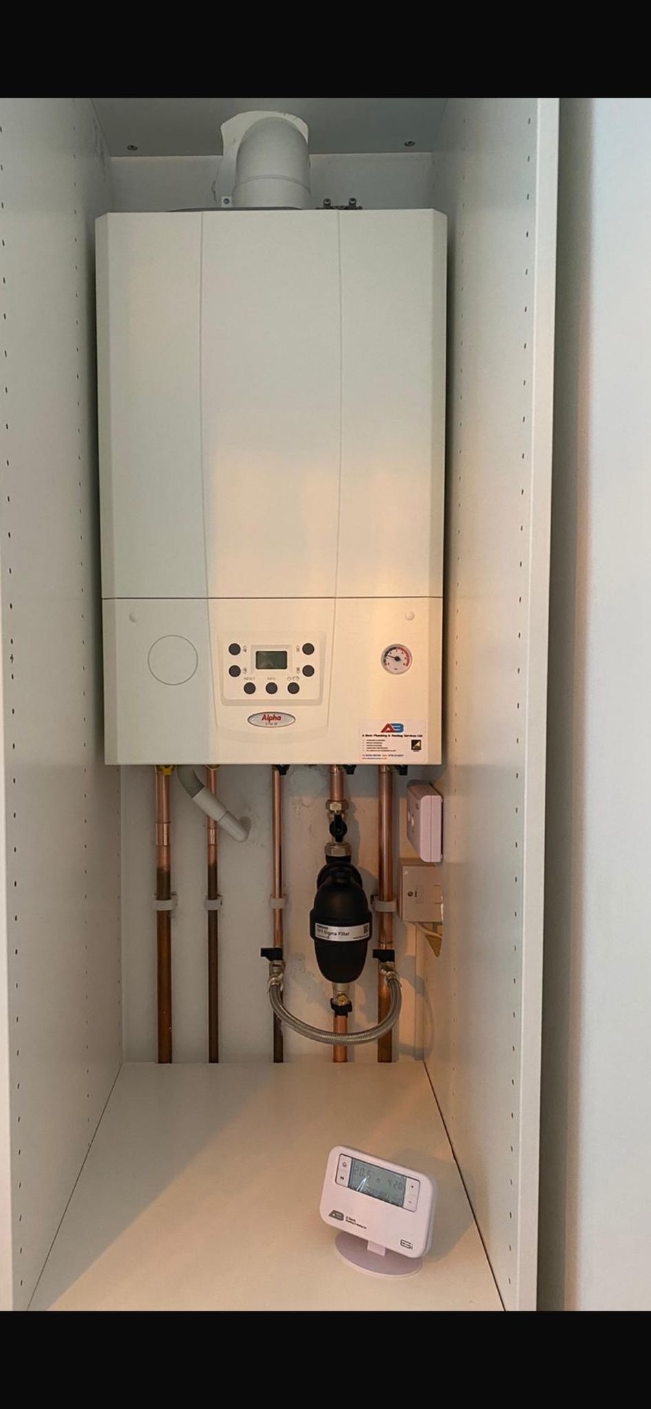 A white boiler inside a cabinet with copper pipes and a thermostat.