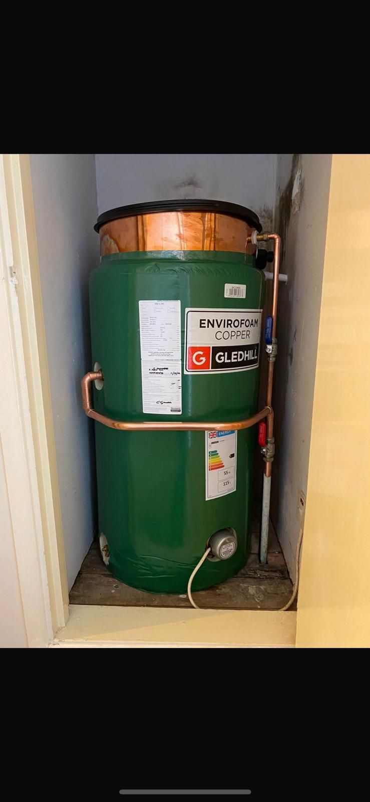 A green hot water tank with copper piping in a recessed alcove.