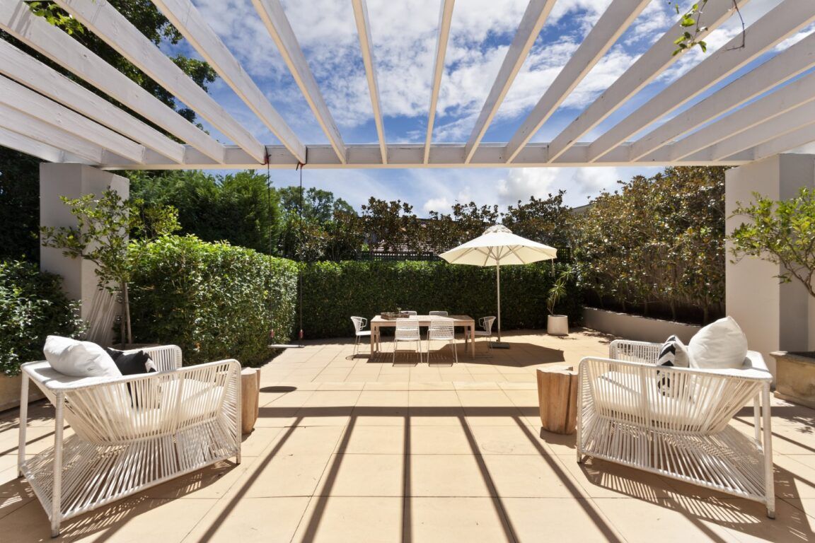 A Patio With Chairs and an Umbrella Under a Pergola — Lakecrest Projects in Lake Macquarie, NSW