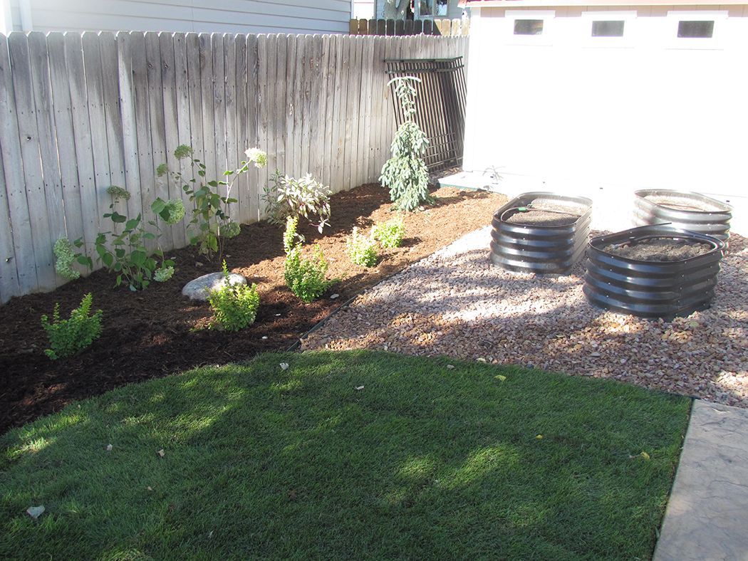 Backyard with fence, garden bed, lawn, and stacked black planters.