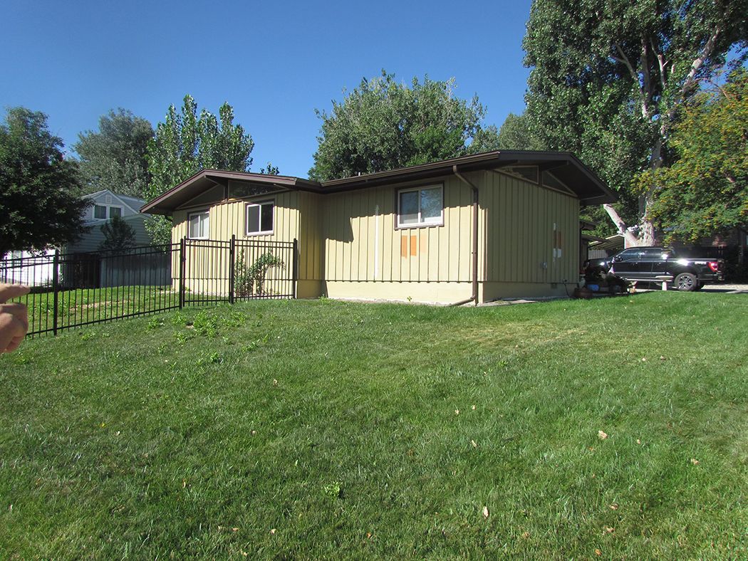 Yellow-sided bungalow with small yard and short fence, trees, and car parked on the side.
