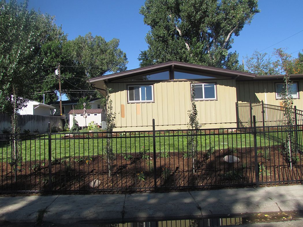 Beige house behind a black metal fence, with trees and blue sky.