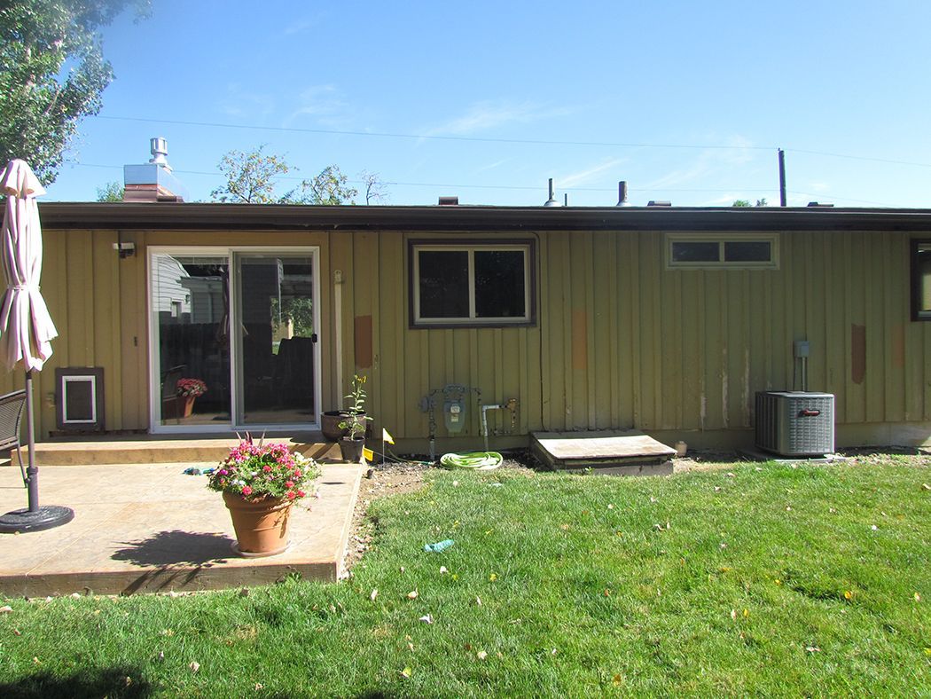 Backyard view of a house with a sliding glass door, patio, grass, and blue sky.