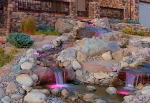 A rocky waterfall feature with colorful illuminated water flowing into a small pond.