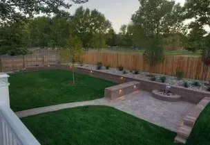 A landscaped backyard with a brick patio, fountain, and green lawn surrounded by a wooden fence.