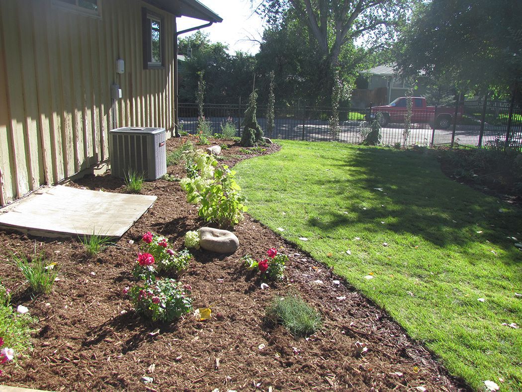 A landscaped yard with a flower bed and lush grass, next to a house.