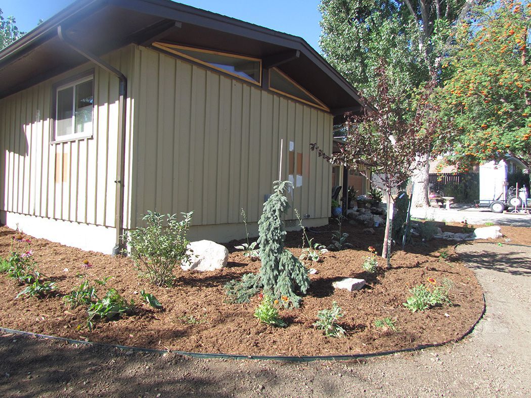 A tan building with a small garden bed, bordered by mulch, next to a gravel pathway.