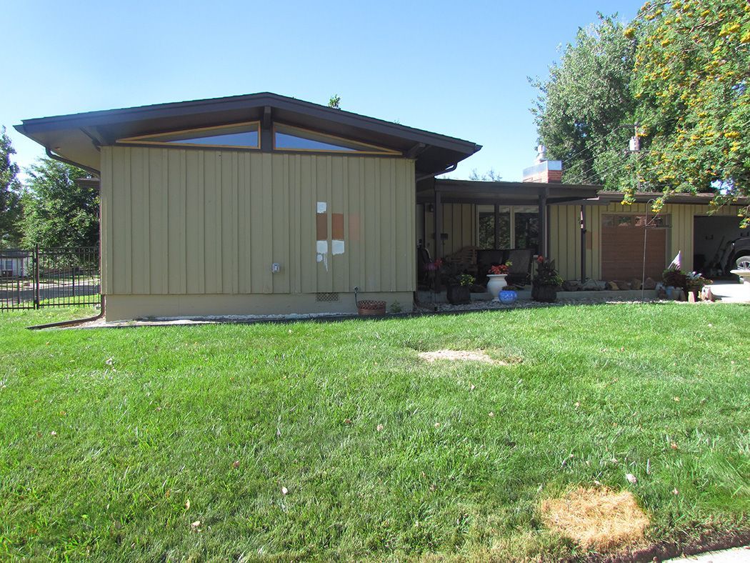 Tan mid-century modern house with a gabled roof and a green lawn.