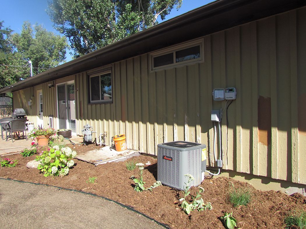 Exterior view of a house with siding and an air conditioner, brown mulch and a small garden.