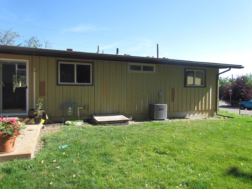 Backyard view of a single-story house with green siding, grass, and blue sky.