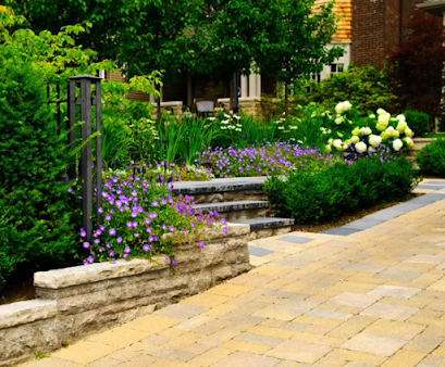 Stone steps lead to a lush garden with purple flowers, green bushes, and a paved path.