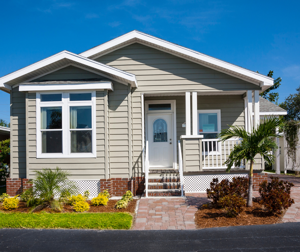 A picture of a tan house with a porch and a garden in front.