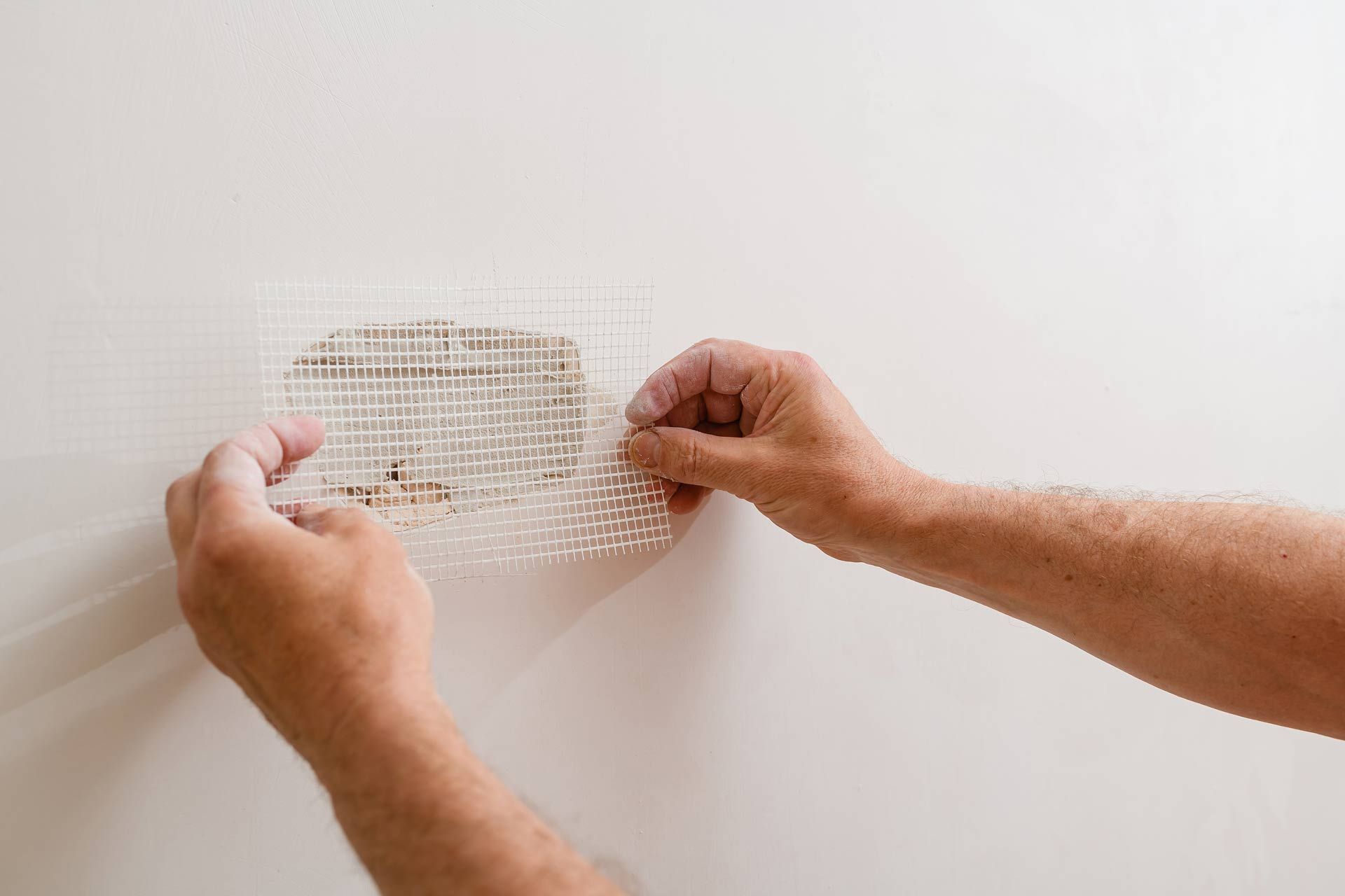 Hands placing mesh over a damaged section of a white wall, preparing for repair.
