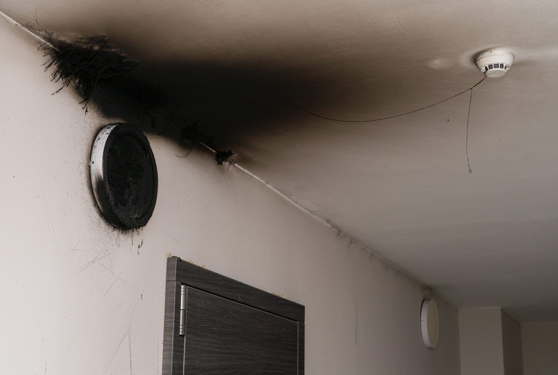 Smoke damage on a white ceiling and wall, near a vent and a smoke detector.