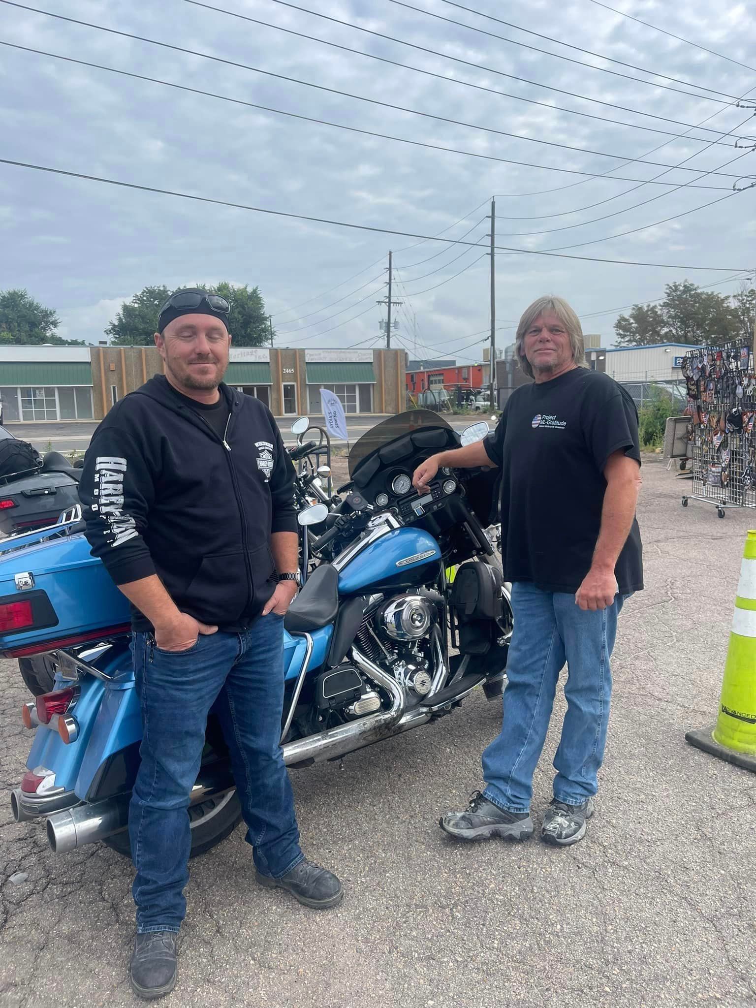 Two men are standing next to a blue motorcycle in a parking lot.
