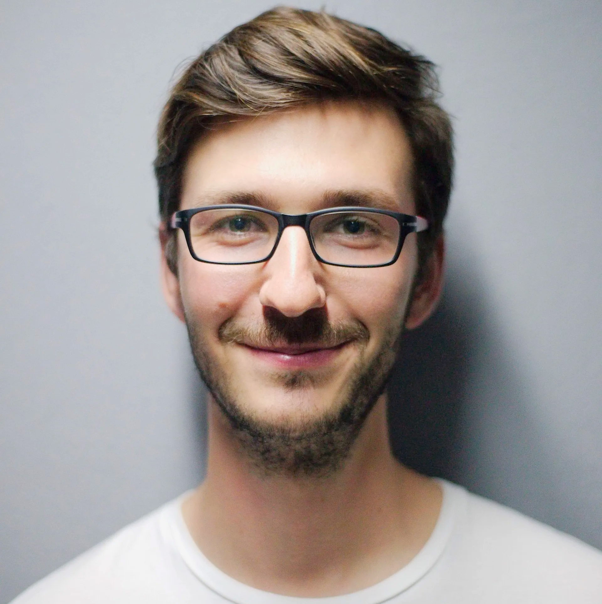 A man wearing glasses and a white shirt smiles for the camera