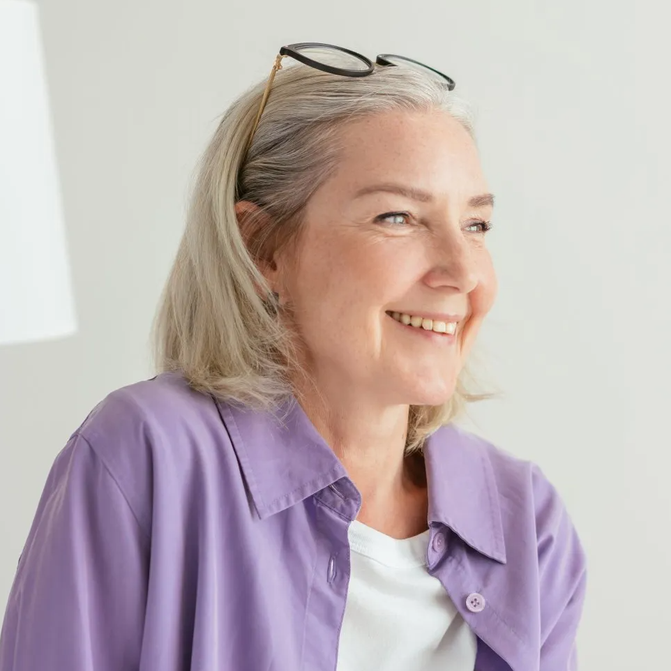 A woman wearing glasses and a purple shirt is smiling.