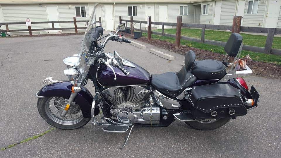 A purple motorcycle is parked in a parking lot in front of a house.