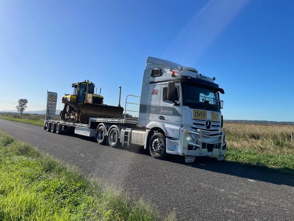 A Semi Truck Is Driving Down A Road With A Bulldozer On The Trailer — Armour Transport Logistics In Mackay, QLD