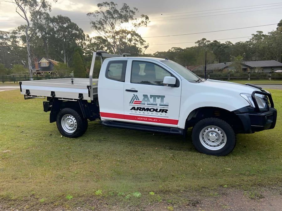 A White Truck With A Flat Bed Is Parked In A Grassy Field — Armour Transport Logistics In Maitland, NSW