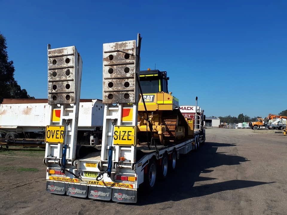 A Truck With A Yellow Bulldozer On The Back Is Parked In A Parking Lot — Armour Transport Logistics In Singleton, NSW