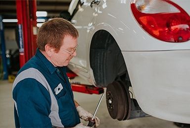 Mechanic working on the wheel of a white car in a garage, using a screwdriver. | Emge's Car Craft Auto Services