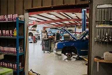Open garage with cars on lifts; mechanics working, tools and parts visible. | Emge's Car Craft Auto Services