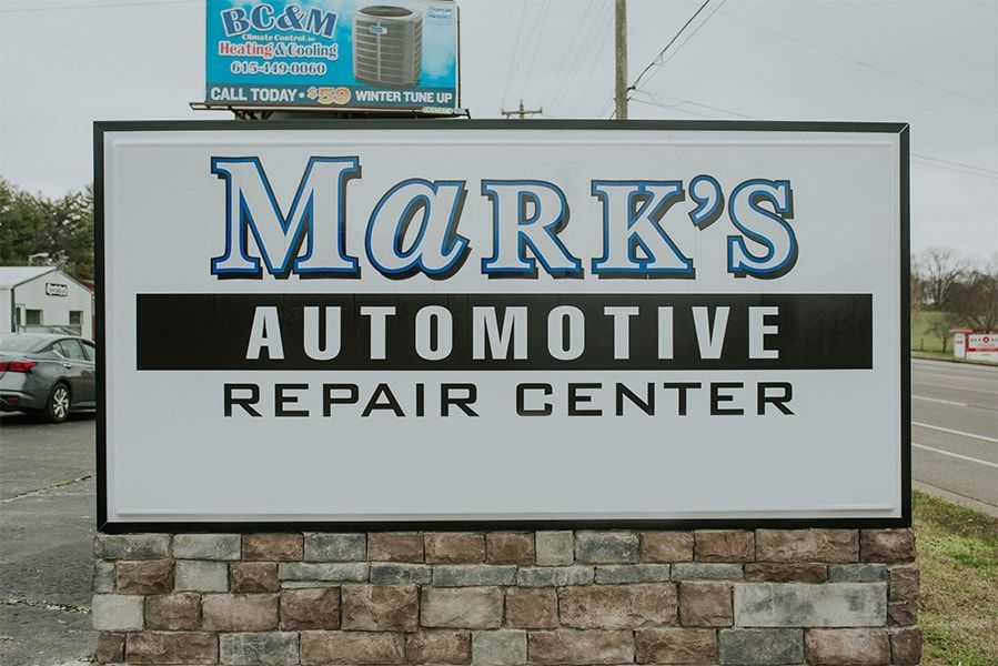 Sign for Mark's Automotive Repair Center with blue and white lettering against a stone base. | Emge's Car Craft Auto Services
