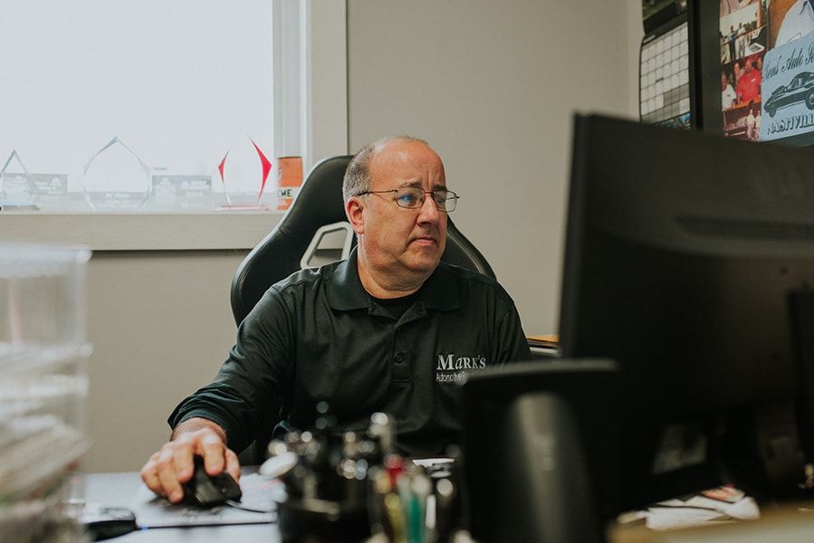Man in black shirt at a desk, looking at a computer, holding a mouse. Office setting. | Emge's Car Craft Auto Services