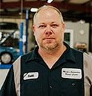 Mechanic in blue and gray work shirt, standing in a garage, looking at the camera. | Emge's Car Craft Auto Services