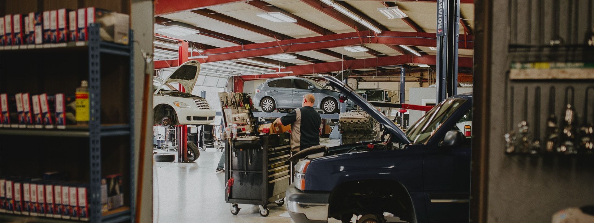 Interior of a car repair shop with several vehicles, tools, and a person working on a car. | Emge's Car Craft Auto Services