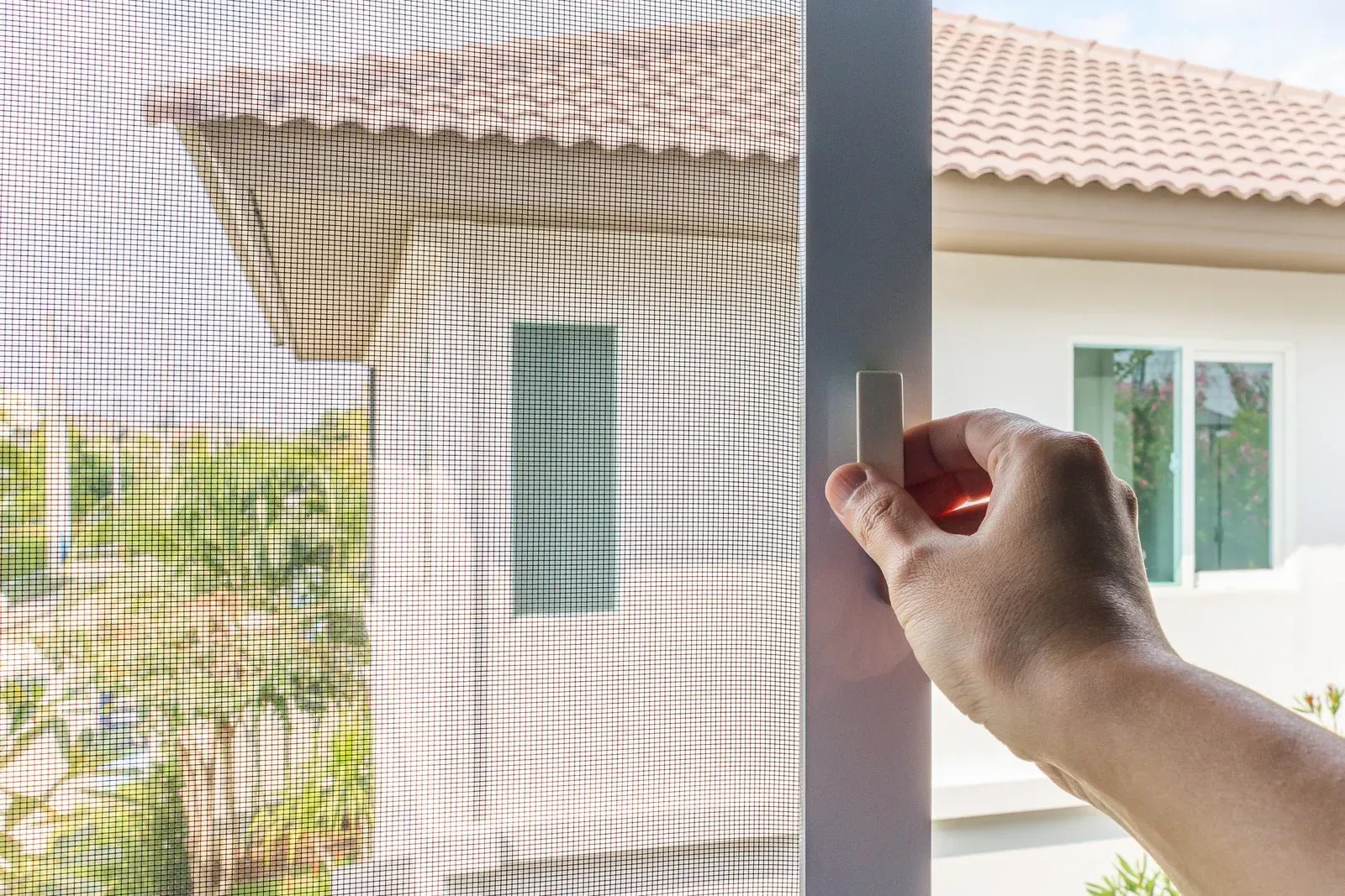 A person is opening a screen door to a house.