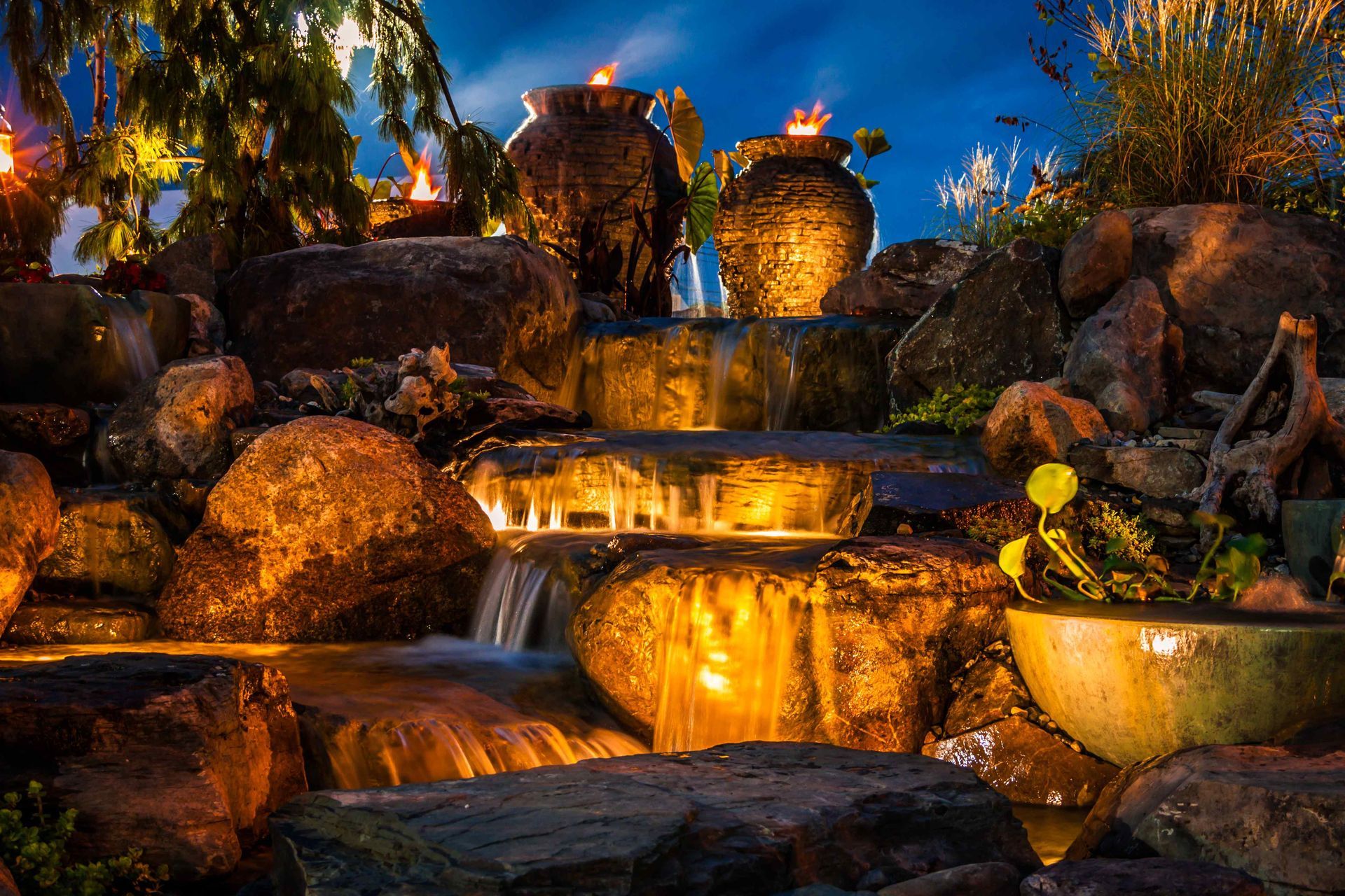 A cascading landscape water feature with ceramic pots and basins illuminated dramatically from below