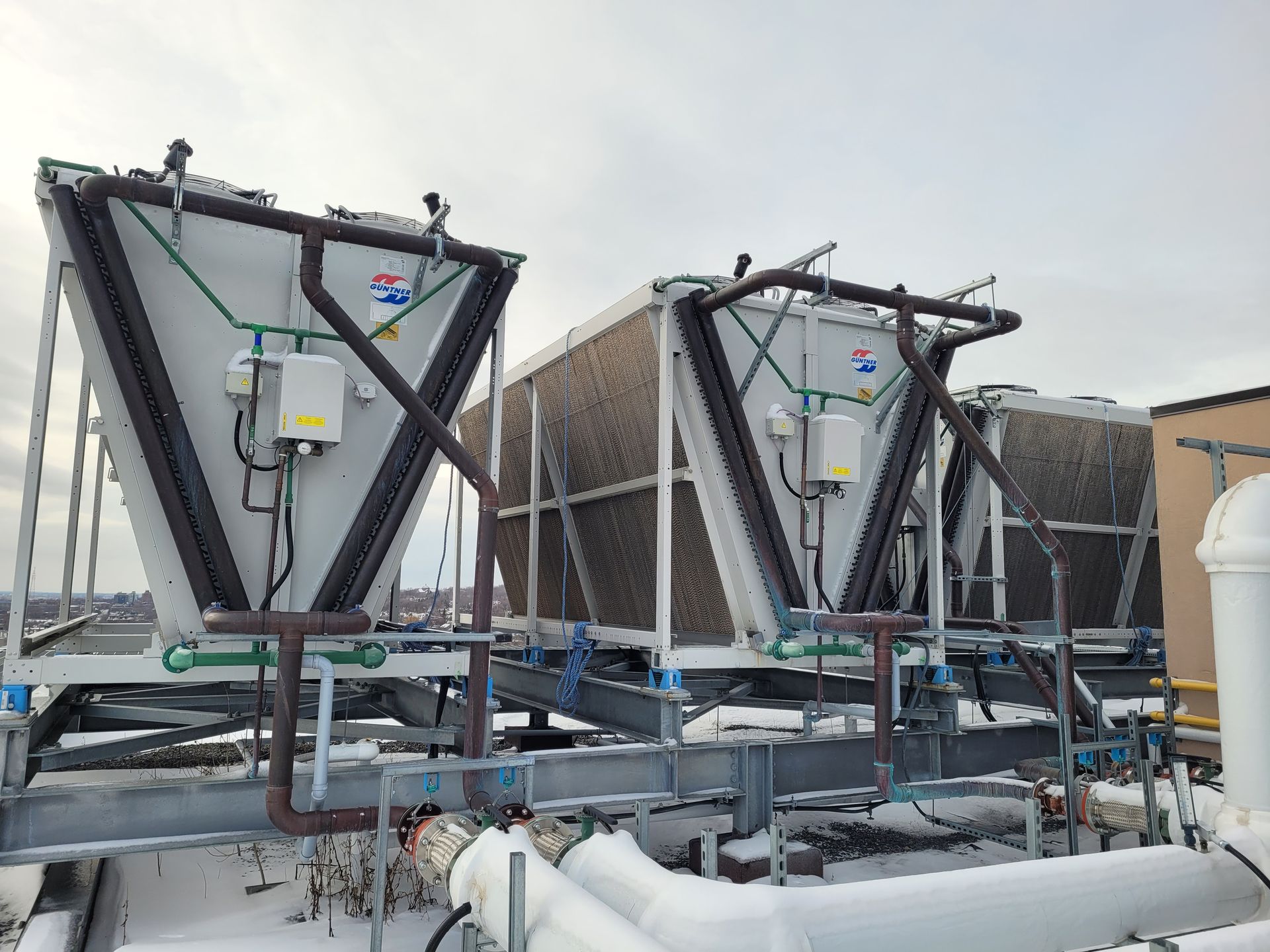 Une rangée de tours de refroidissement est posée sur un toit recouvert de neige.