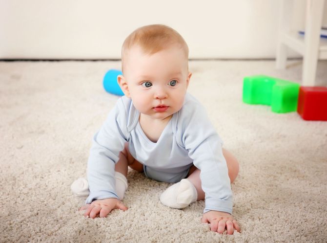 Un bambino gattona su un tappeto con giocattoli colorati sullo sfondo.