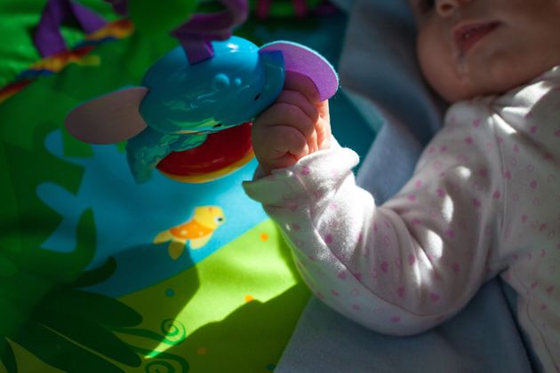 Un bambino tiene in mano un giocattolo colorato mentre è sdraiato su un tappetino da gioco dai colori vivaci.