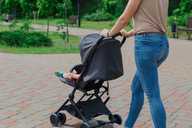Adulto che spinge un passeggino nero su un sentiero di mattoni in un parco verde