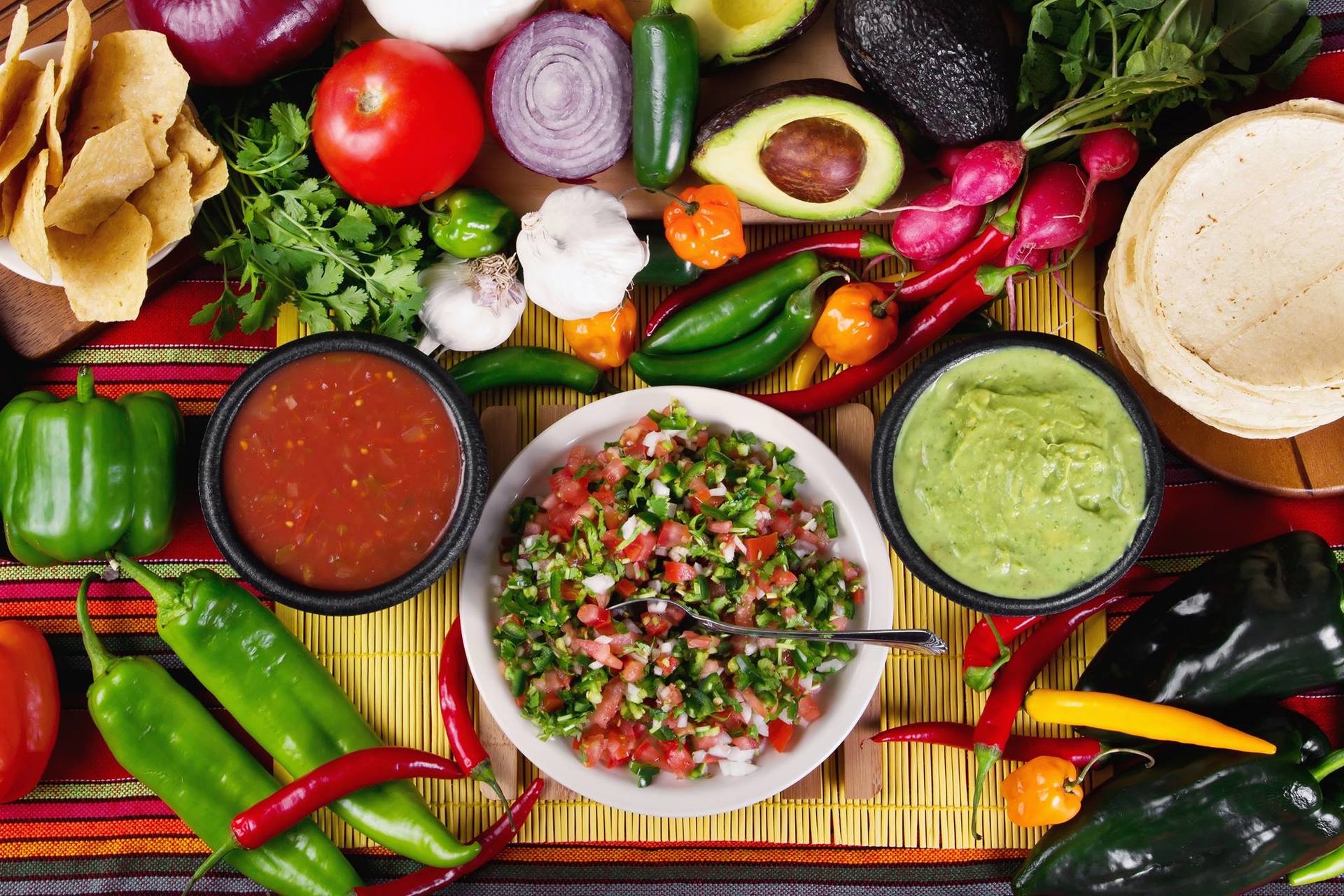 Colorful Mexican food spread with salsa, guacamole, tortillas, chips, and fresh vegetables.
