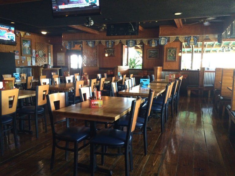 Interior of a restaurant with wooden tables and chairs, dim lighting, and TVs on the walls.